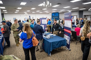 A wide view of a conference room filled with a variety of people, service members in uniform and business casual attire
