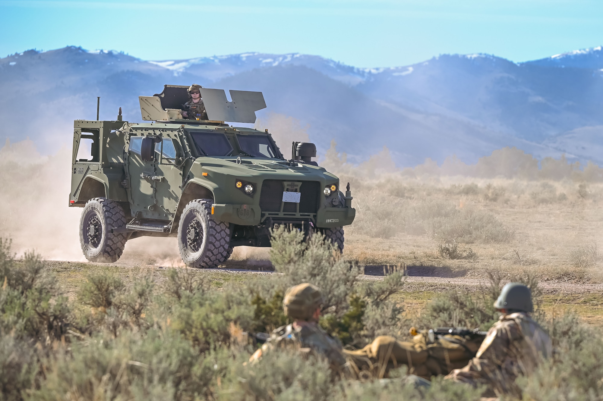 Joint Light Tactical Vehicle driving. Two airmen prone on the ground.