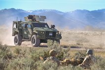Joint Light Tactical Vehicle driving. Two airmen prone on the ground.
