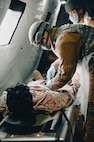 Two Airmen with masks and gloves inside a tent patting down a simulated injured dummy