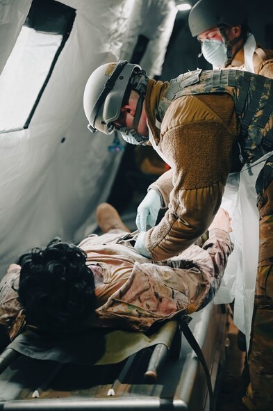 Two Airmen with masks and gloves inside a tent patting down a simulated injured dummy
