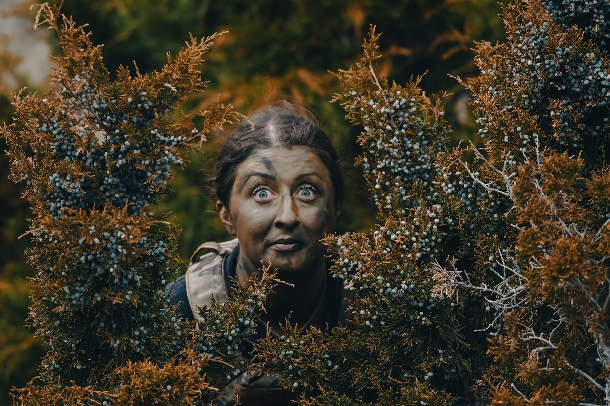 Airman covered in camouflage face paint behind bushes