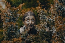 Airman covered in camouflage face paint behind bushes