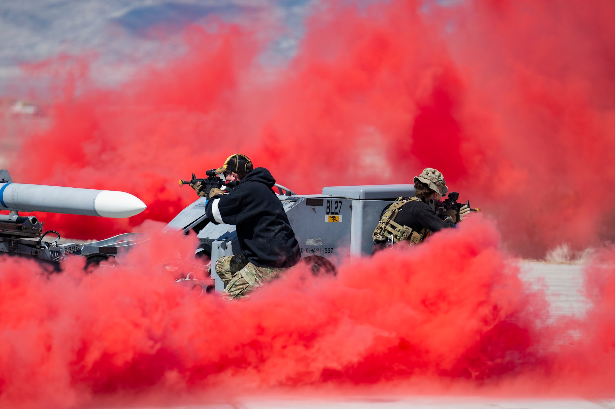 A photo of Airmen shooting through a cloud of red smoke