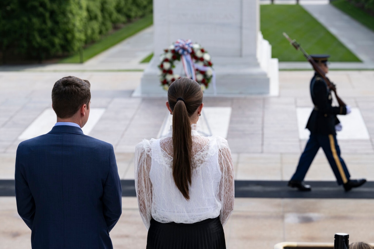 A couple watch a soldier march past a marker.