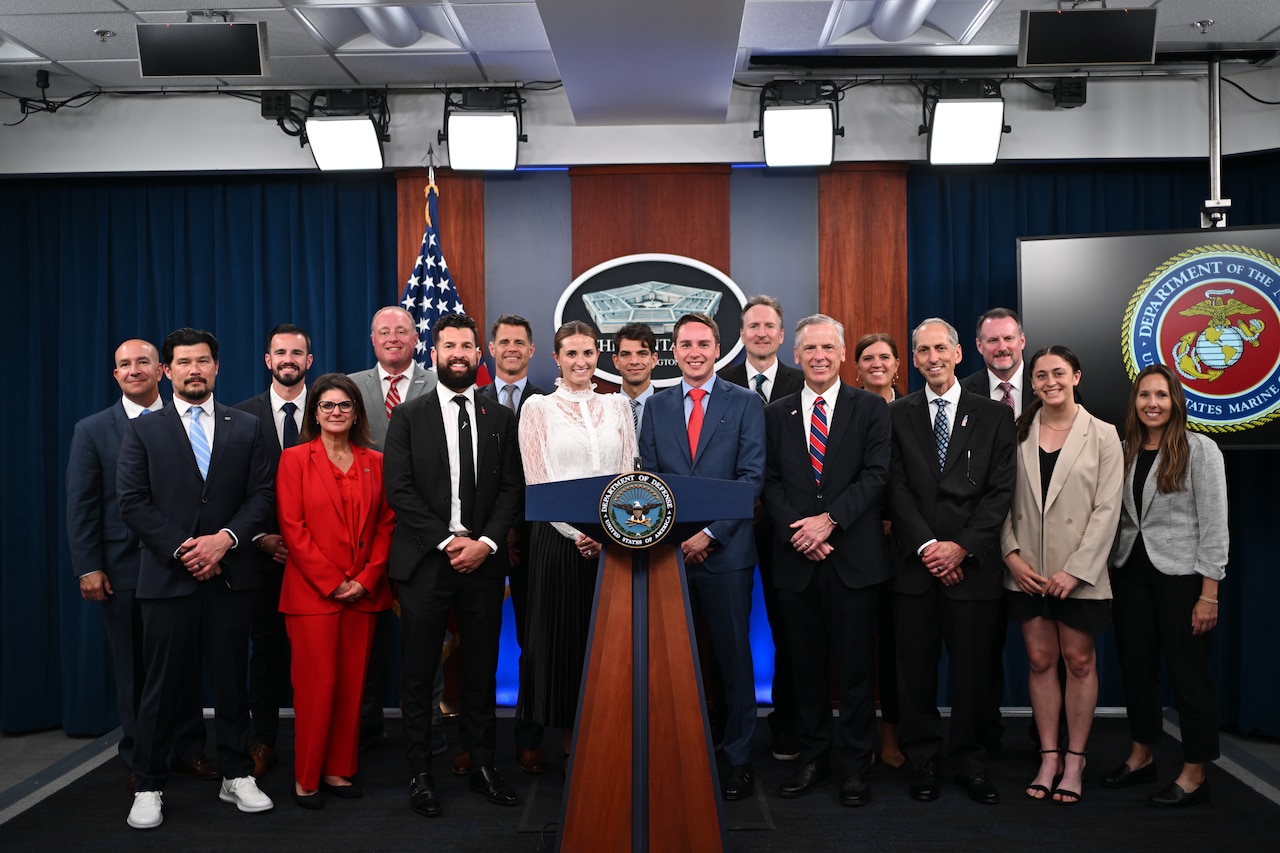 A group poses for a photo in a briefing room at the Pentagon.
