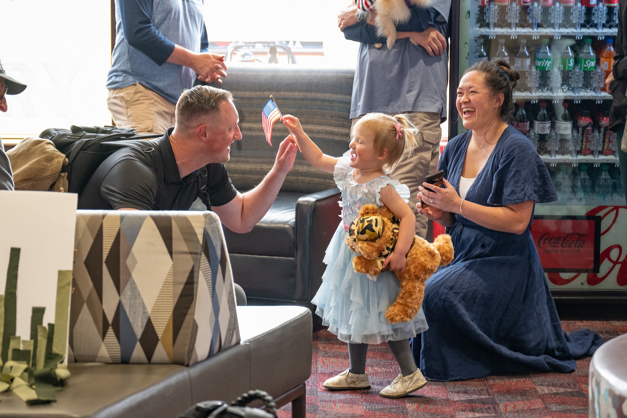 A little girl raises an American flag at a man while a woman laughs behind her.