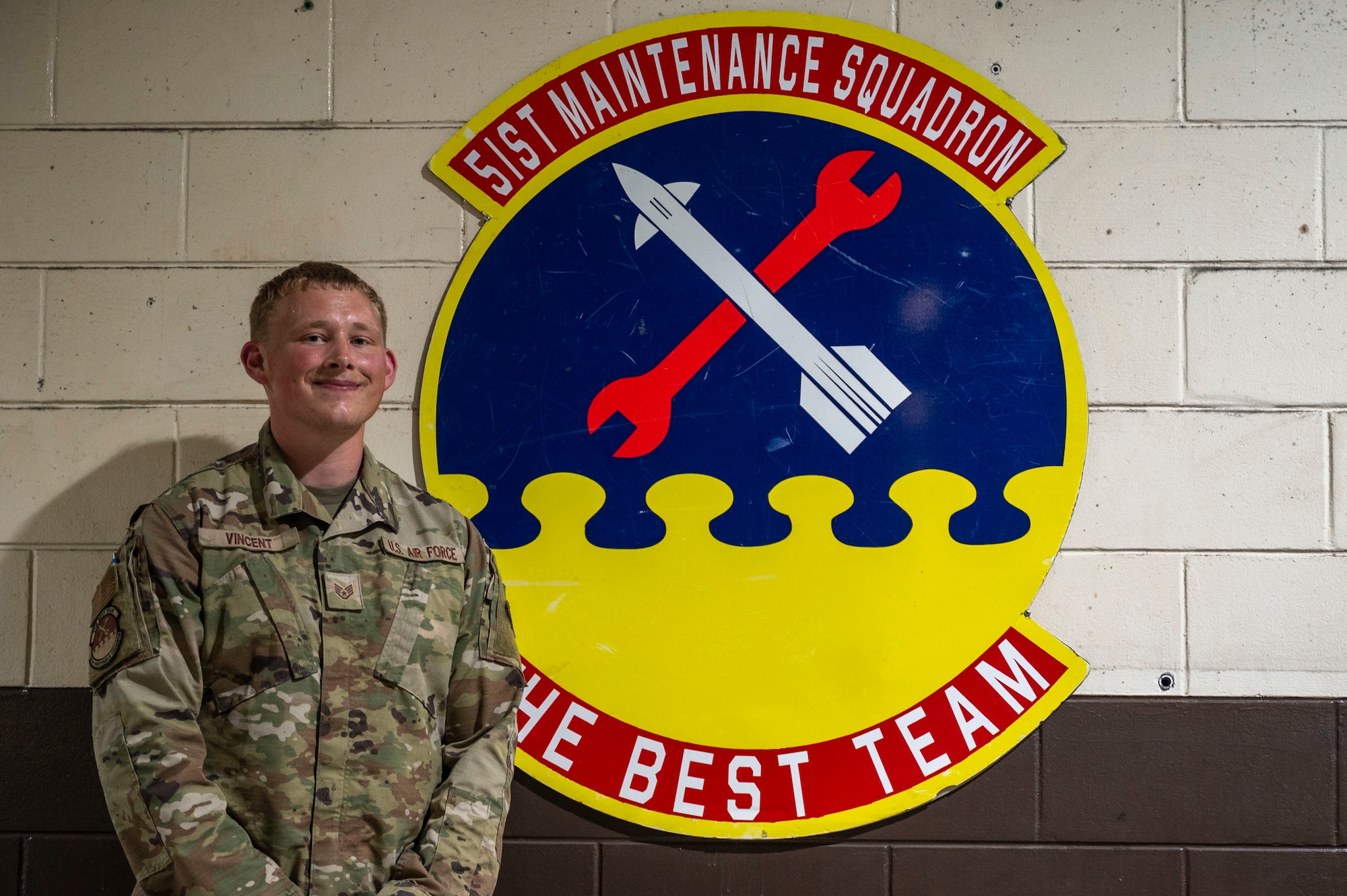 U.S. Air Force Staff Sgt. Bryce Vincent, 51st Maintenance Squadron corrosion control lead, poses next to his shop’s emblem at Osan Air Base, Republic of Korea, July 31, 2025.