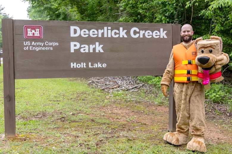 Russell Barton, U.S. Army Corps of Engineers, Mobile District Holt Resource Office Park Ranger, poses in front of the sign at Deerlick Creek Park in his Bobber the Water Safety Dog suit Tuscaloosa, Alabama, April 25, 2025. Bobber the Water Safety Dog promotes water safety and the wearing of life jackets to children and families to keep them safe on the water. (U.S. Army photo by Travis England)