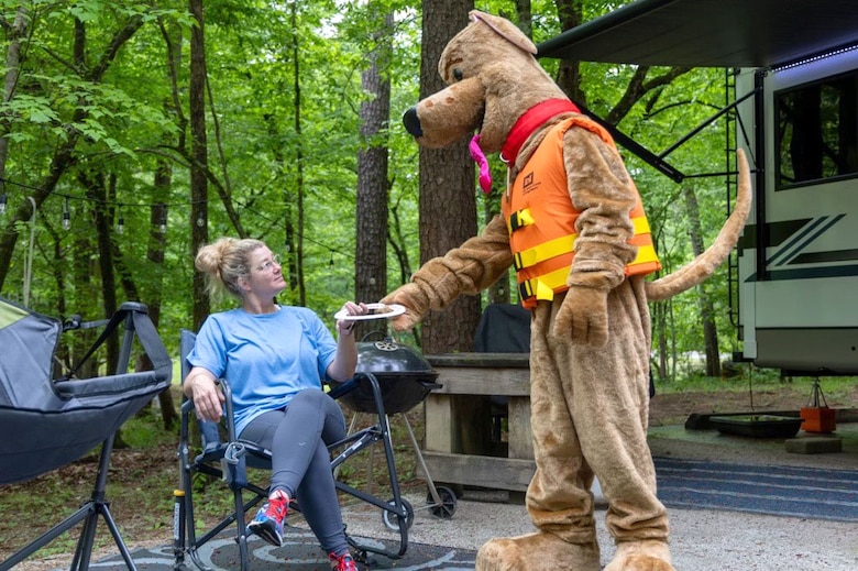 Bobber the Water Safety Dog hands a water safety brochure to a camper at Deerlick Creek Park, Tuscaloosa, Alabama, April 25, 2025. Bobber, who was created by the National Water Safety Program in 2003, plays an integral role in promoting water safety at U.S. Army Corps of Engineers Parks, rivers and lakes. (U.S. Army photo by Travis England)