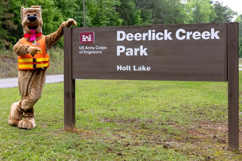 Bobber the Water Safety Dog poses in front of the sign of the entrance to Deerlick Creek Park, Tuscaloosa, Alabama, April 25, 2025. Russell Barton, the USACE Ranger who portrays Bobber for the Mobile District, said he loves promoting water safety and having fun and interaction with the kids as he portrays and helps to educate them as Bobber. (U.S. Army photo by Travis England)