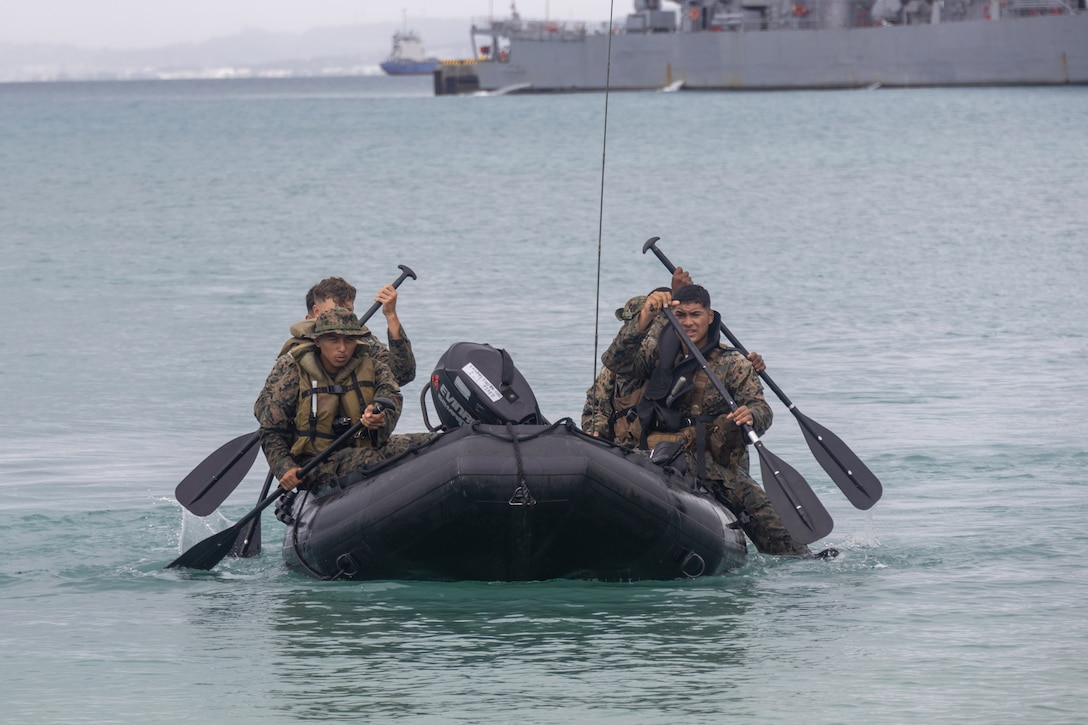 Four Marines in a small rubber boat each use a paddle to propel the craft forward on the ocean.