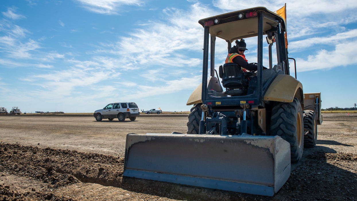 Construction crew working on flight line with backhoe loader