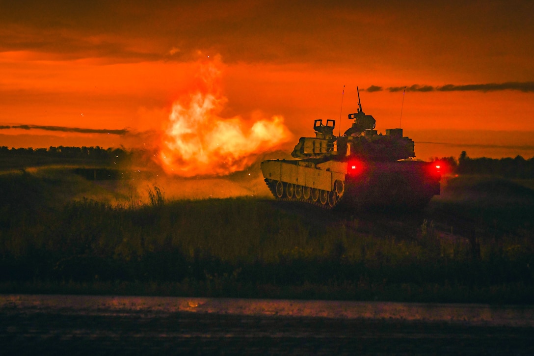 Flames emerge as a tank fires in a field under a red sky.