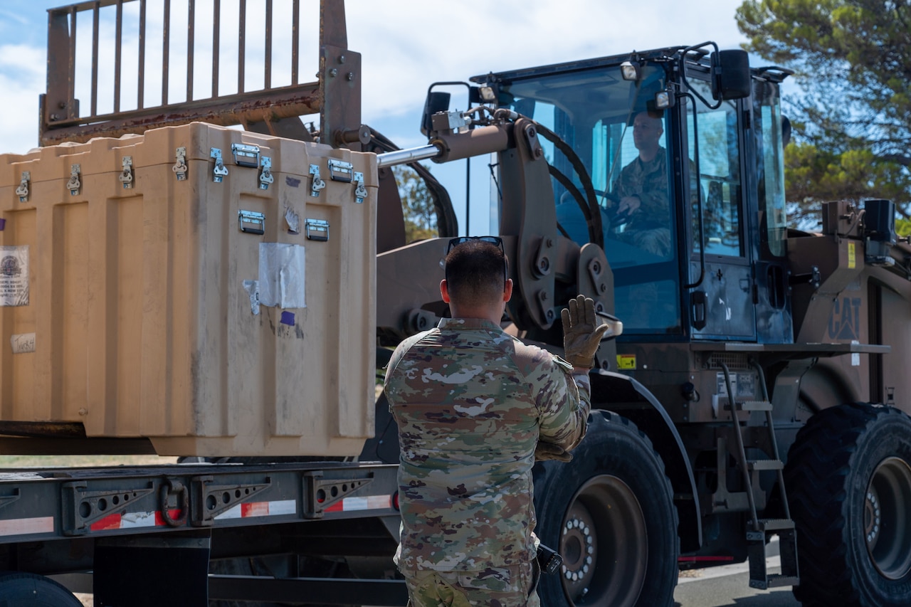Airmen in camouflage uniforms offload a small shipping container from a flatbed truck.