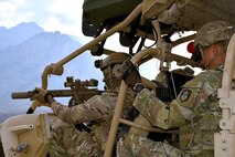two soldiers sit in a military vehicle with guns drawn