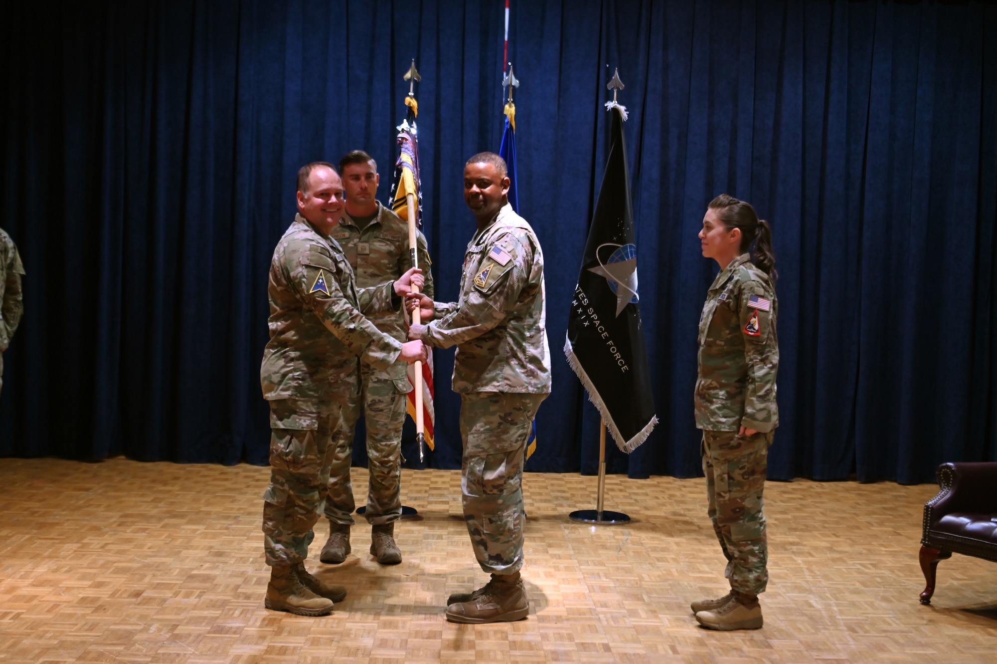 three people stand on a stage and pass a guidon