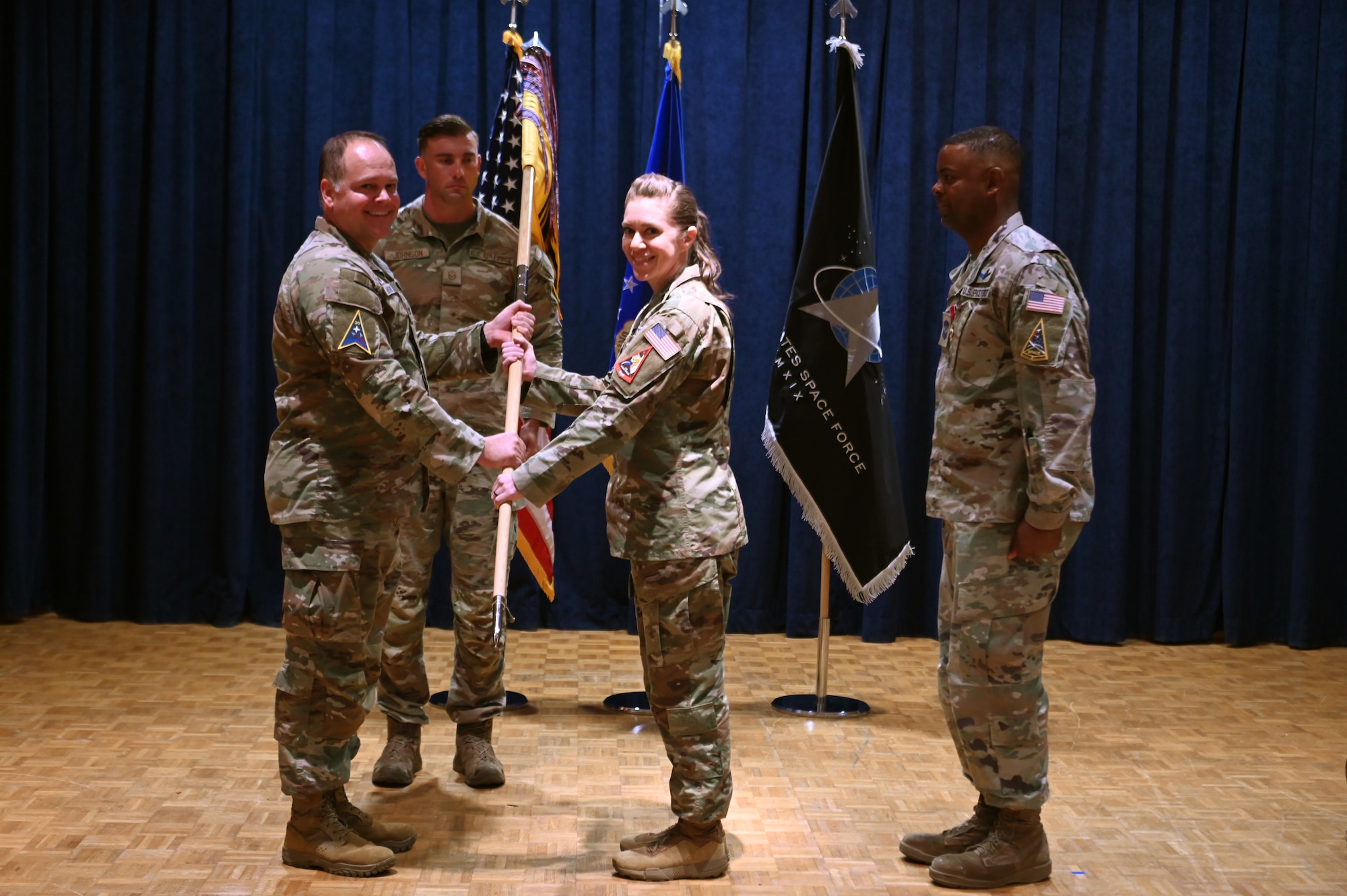 three people stand on a stage and pass a guidon
