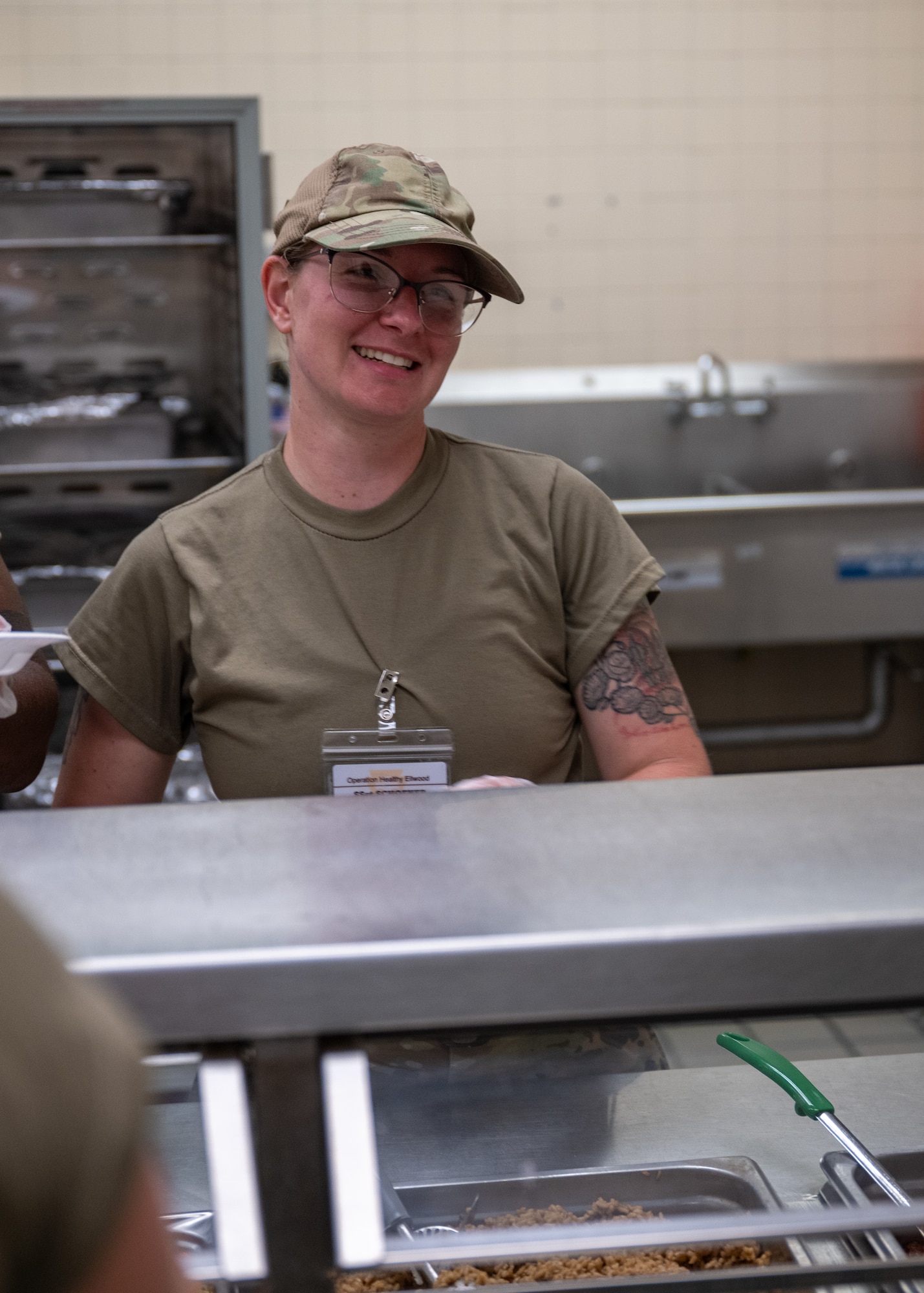 A woman in military attire laughs while serving food.