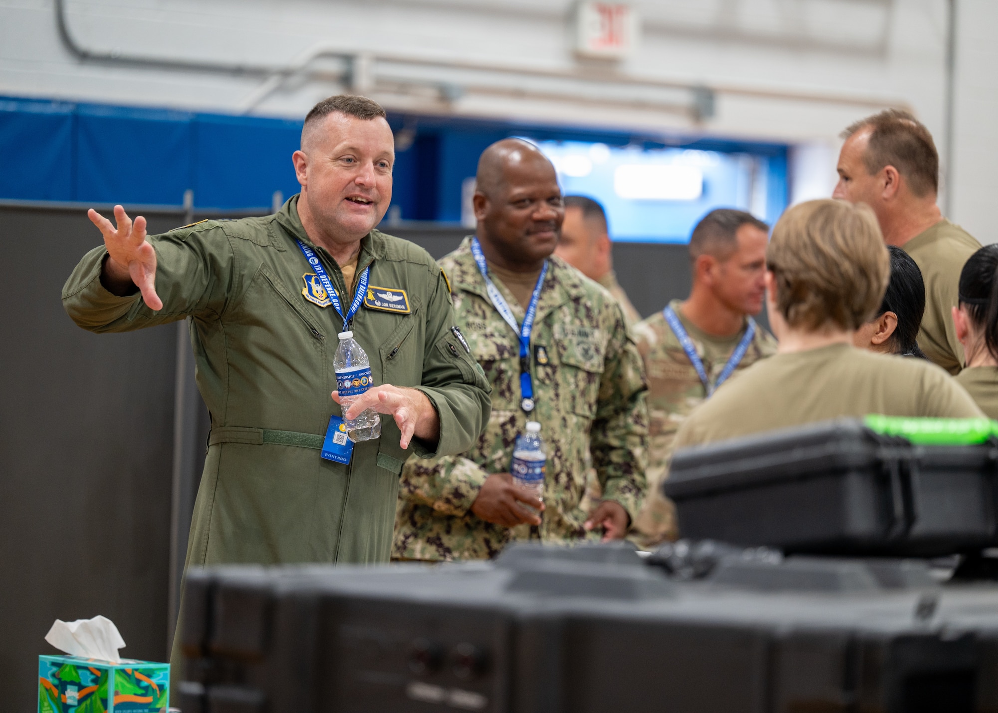 A man in a military flight suit talks to other service members.