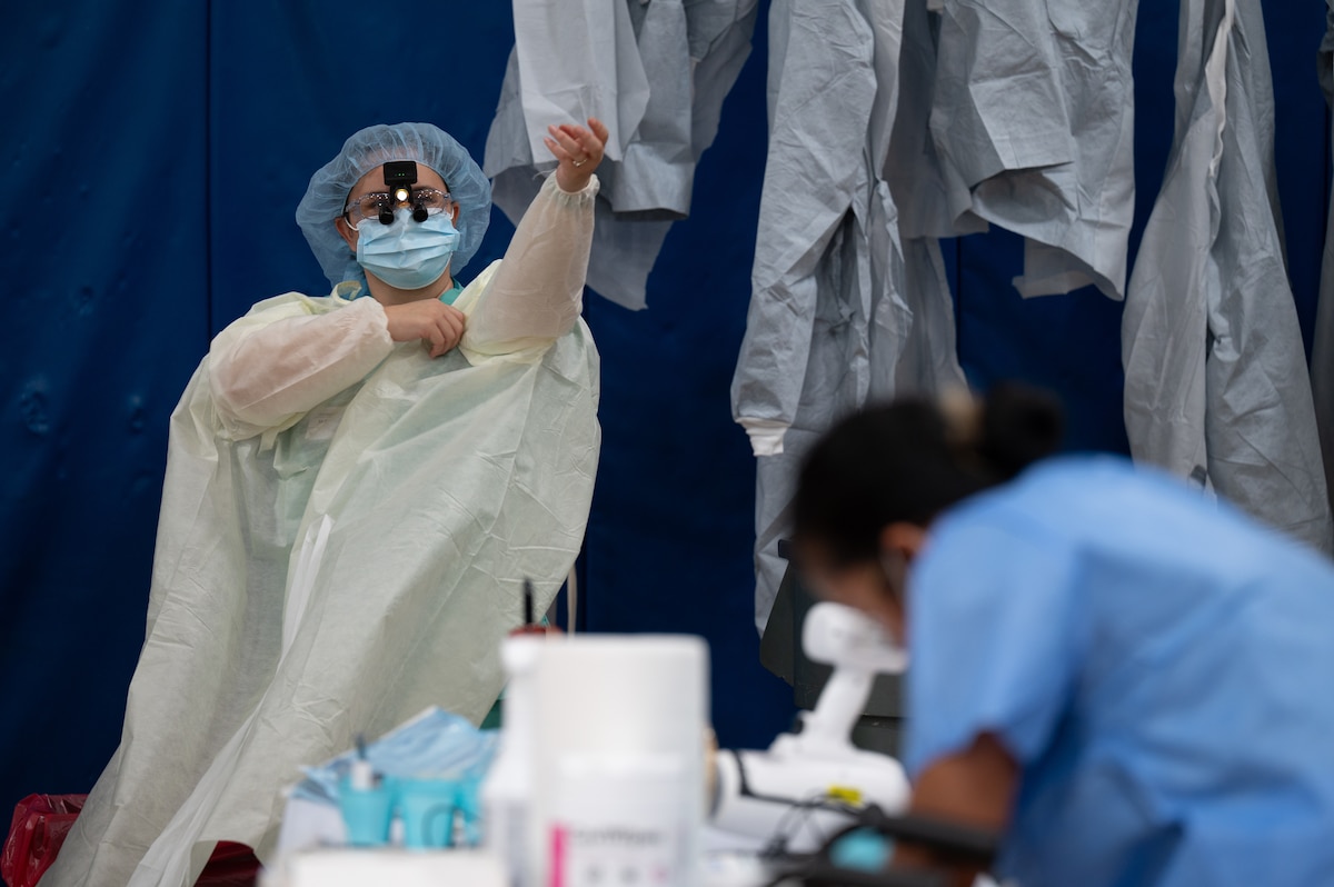 A person dons protective medical gear while sitting on a stool in a school gymnasium.