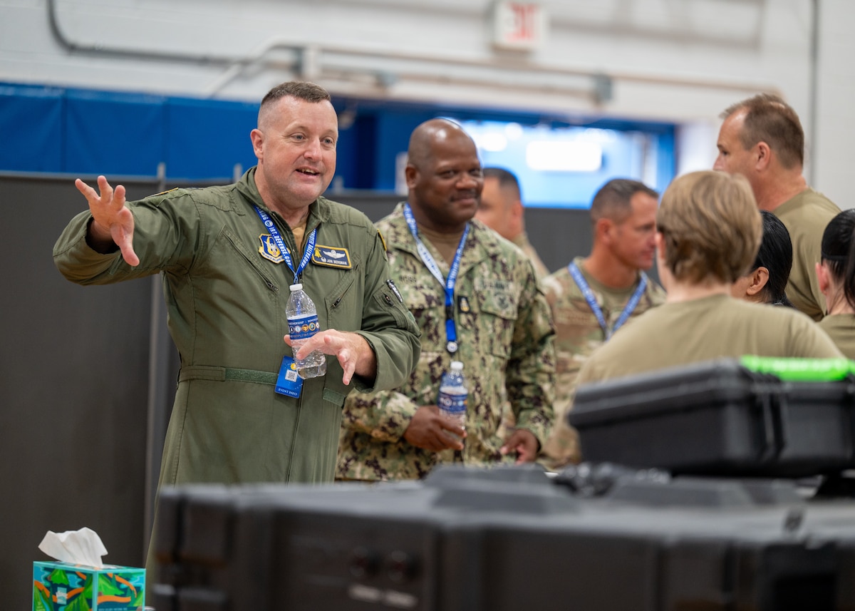 A man in a military flight suit talks to other service members.