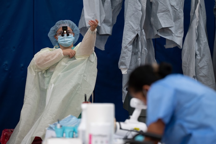 A person dons protective medical gear while sitting on a stool in a school gymnasium.