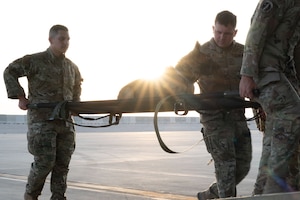 From the left, U.S. Air Force Staff Sgt. Jesus Sanchez, 379th Expeditionary Security Forces Squadron military working dog handler, MWD Kicsi, and Staff Sgt. Jacob Dick, 379th ESFS MWD handler, practice litter carries within the U.S. Central Command area of responsibility July 17, 2025.MWDs play a vital role in maintaining security by undergoing extensive training to detect explosives and respond to threats. (U.S. Air Force photo by Senior Airman Dieondiere Jefferies)