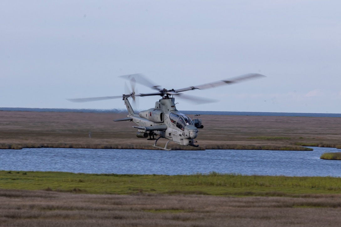 A U.S. Marine Corps AH-1W Super Cobra with Marine Medium Tiltrotor Squadron 263, Marine Aircraft Group 26, 2nd Marine Aircraft Wing, flies over a training site during exercise Burmese Chase 25 at Bombing Target 11, Piney Island, North Carolina, July 31, 2025. Burmese Chase is an annual U.S. led, multi-lateral training exercise comprised of integrating ground and air fires, infantry tactics and naval gunfire alongside NATO allies to enhance combat readiness and interoperability. (U.S. Marine Corps photo by Cpl. Marc Imprevert)