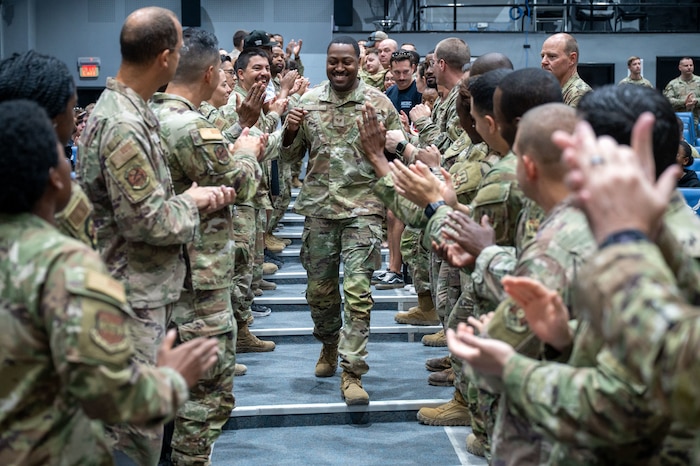 SSgt Lee walks middle frame down an aisle with Airmen on either side of him with fist bumps, high-fives and handshakes