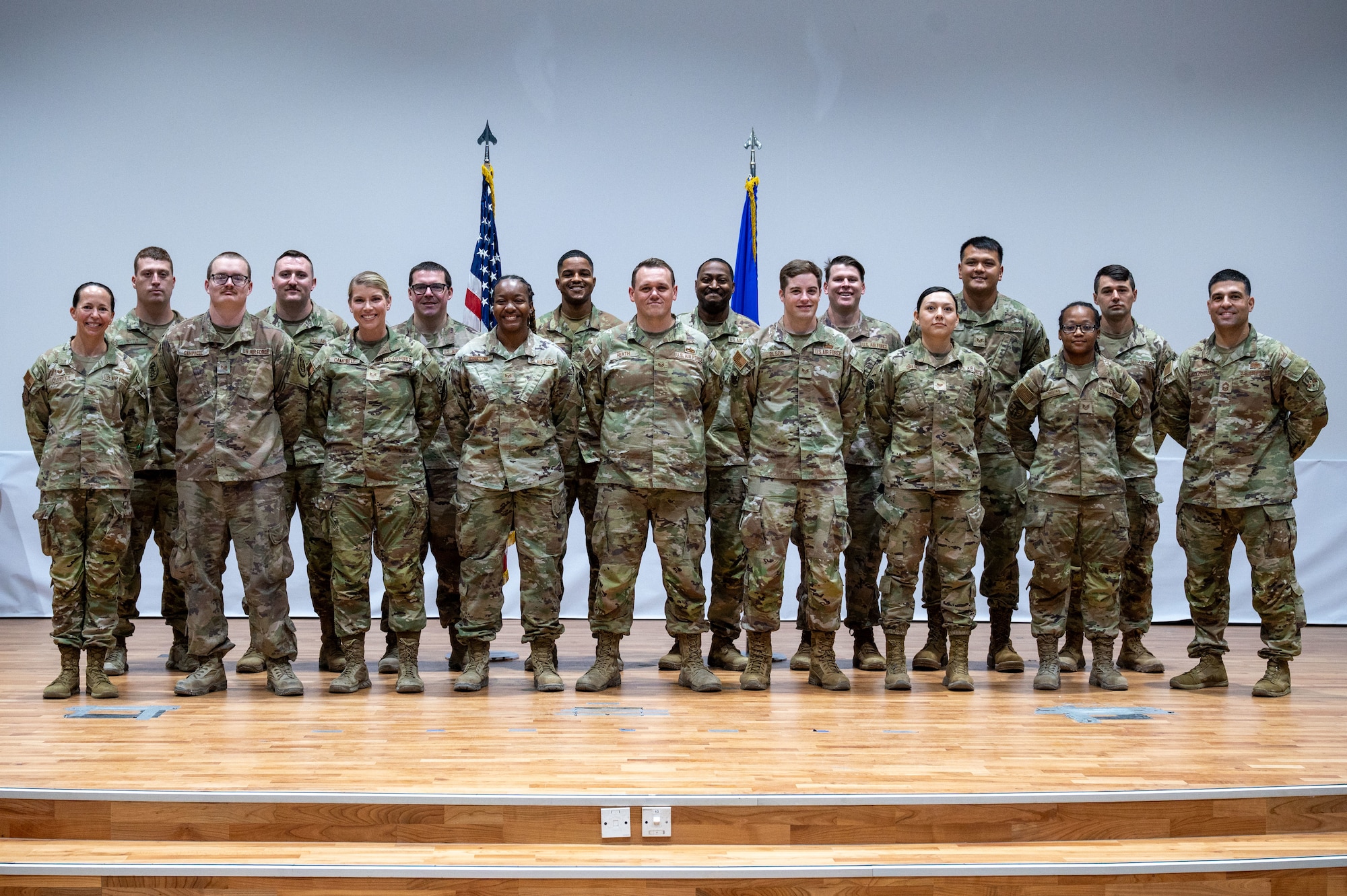 A group of SSgt selects and 386th EABG senior leadership in two rows pose in front of flags at parade rest