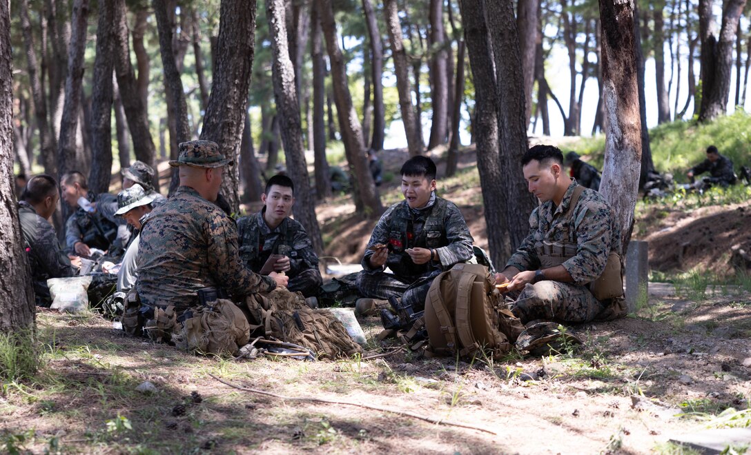 U.S. Marines with 2nd Battalion, 23rd Marines, forward deployed with 4th Marine Regiment, 3d Marine Division as part of the Unit Deployment Program, and Republic of Korea Marines with 1st Marine Division, ROK Marine Corps, talk and share their Meals Ready-to-Eat during the Korean Marine Exercise Program 25.2 in Pohang, South Korea, July 28, 2025. KMEP is conducted regularly between the ROK and U.S. Marine Corps to increase their combined capabilities through realistic training geared towards deterrence and maintaining peace in the Indo-Pacific. (U.S. Marine Corps photo by Cpl. Kanoa Thomas)