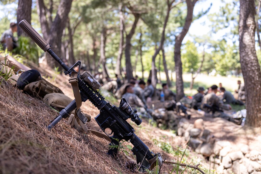 A rifle is staged as the Marines of 2nd Battalion, 23rd Marines, forward deployed with 4th Marine Regiment, 3d Marine Division as part of the Unit Deployment Program, talk and share their Meals Ready-to-Eat with Republic of Korea Marines with 1st Marine Division, ROK Marine Corps, as part of the Korean Marine Exercise Program 25.2 in Pohang, South Korea, July 28, 2025. KMEP is conducted regularly between the ROK and U.S. Marine Corps to increase their combined capabilities through realistic training geared towards deterrence and maintaining peace in the Indo-Pacific. (U.S. Marine Corps photo by Cpl. Kanoa Thomas)