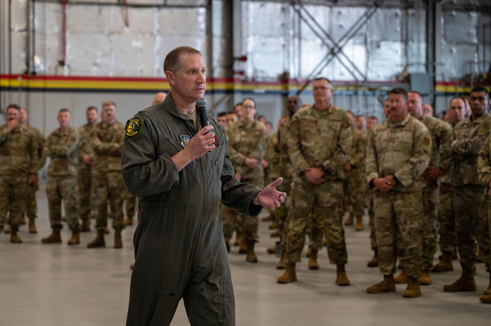 Wing commander gestures while speaking to a group of Airmen