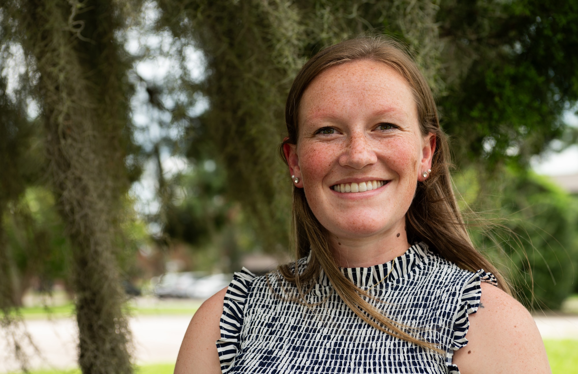 A Caucasian woman poses for a photo in front of a tree on a sunny day in Charleston, South Carolina.