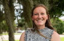 A Caucasian woman poses for a photo in front of a tree on a sunny day in Charleston, South Carolina.