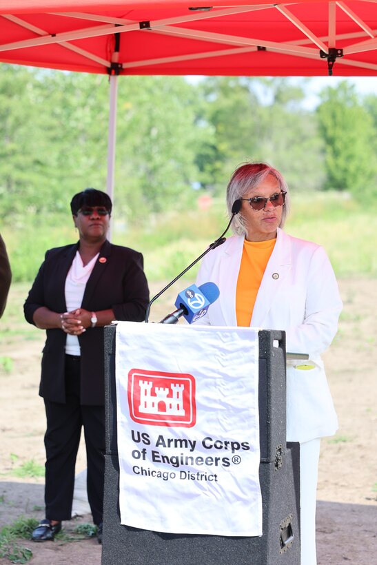 Women stands behind U.S. Army Corps of Engineers podium to give remarks during ribbon cutting ceremony under a red canopy.