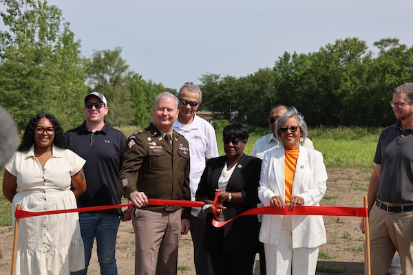 Group stands in front of red ribbon with large scissors during ribbon cutting ceremony.