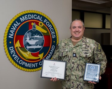 Cmdr. Thomas Sather, director of the Naval Medical Forces Development Command’s Tactical Combat Casualty Care program, displays his recent civilian awards at Joint Base San Antonio-Fort Sam Houston, Texas, Aug. 1, 2025. Sather was presented the American Red Cross Chairpersons’ Award for his significant contributions to the Red Cross Scientific Advisory Council, and recognized the Aerospace Medical Association with the Aerospace Physiology Society’s Fred A. Hitchcock Award for his outstanding performance as a senior aerospace physiologist. (U.S. Navy photo by Malcolm McClendon)