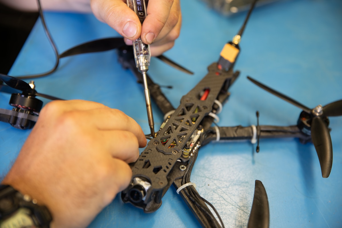 A pair of hands holds a tool and repairs a small drone.