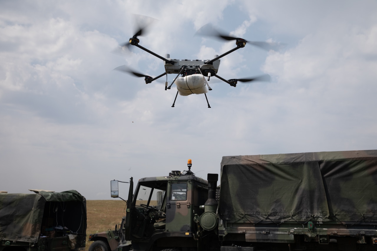 A drone hovers above military vehicles.