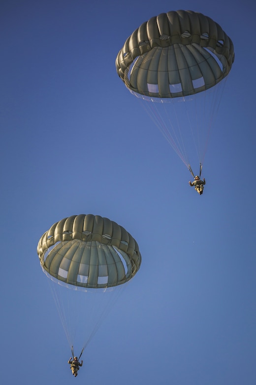 Two paratroopers descend in the sky with their parachutes out on a cloudless day.