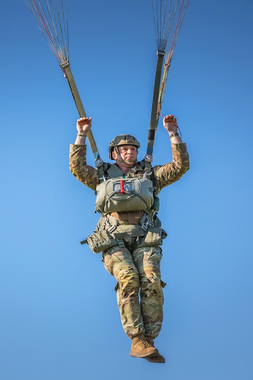 A parachuting soldier descends in a cloudless blue sky.
