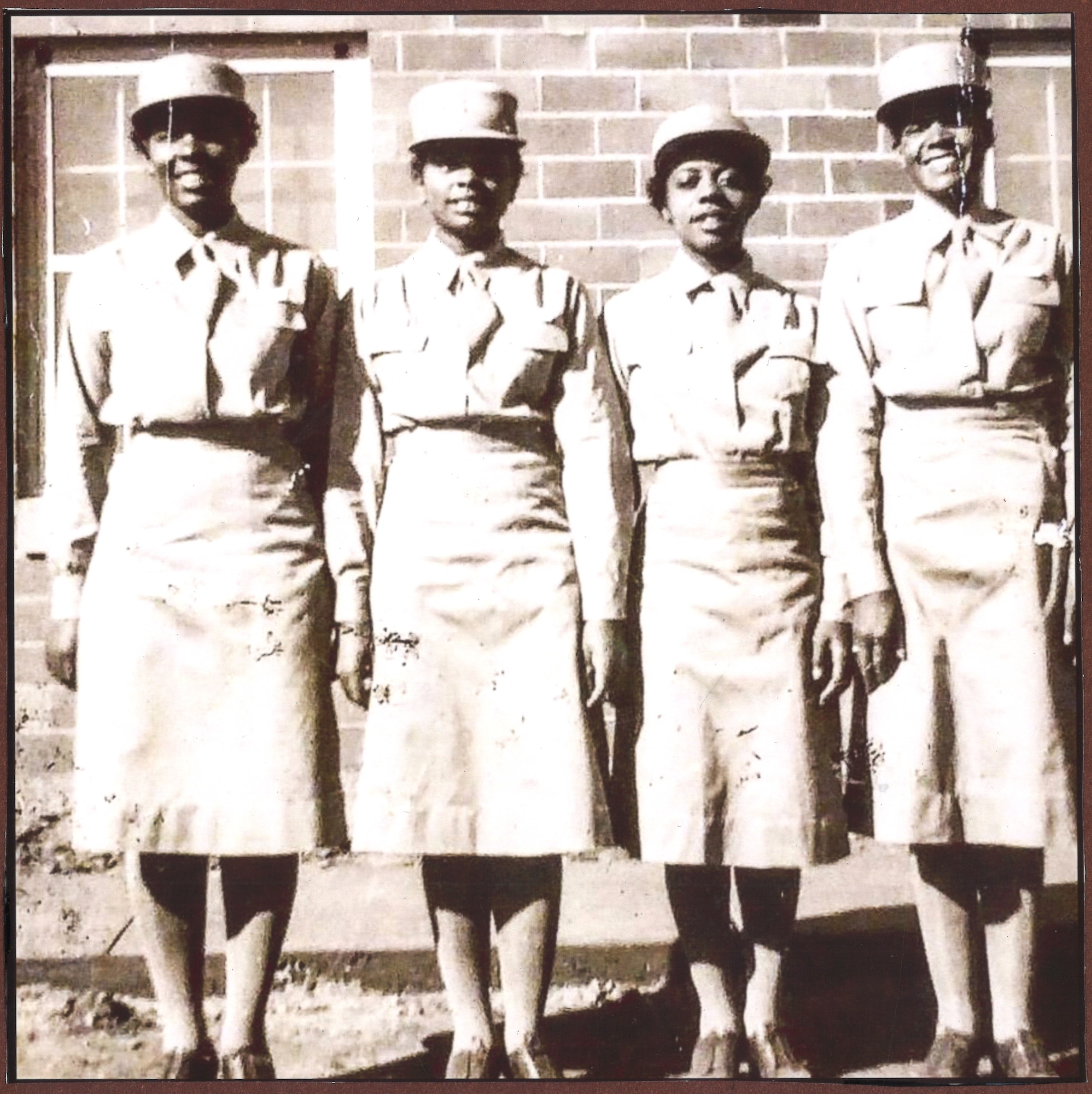 Four women in uniform standing in front of brick building