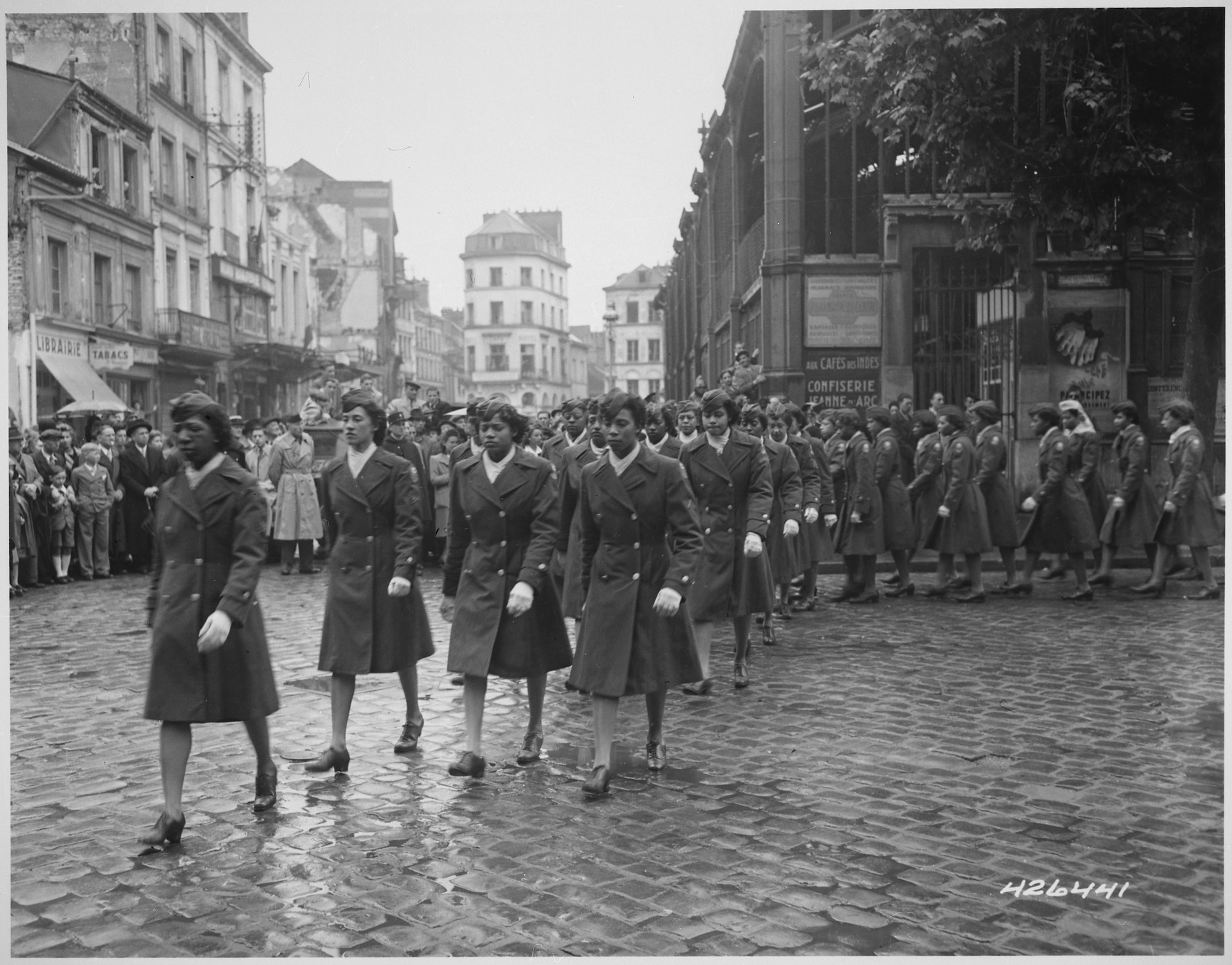 Several rows of women dressed in uniform marching along cobblestone streets in France