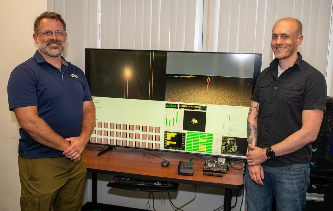 (left) Jonathan King, Naval Surface Warfare Center Panama City Division project and technical execution lead, and Dr. Denton Woods, NSWC PCD scientist, stand next to their latest development the Unmanned Underwater Vehicle Digital Twin Initiative, July 8. This initiative creates realistic, physics-based virtual sonar simulations that allow for critical data collection. These diverse datasets are crucial for validating autonomous systems, target recognition, and change detection technologies, and vital for transitioning advanced technologies into the fleet. (U.S. Navy photo by Ronnie Newsome)