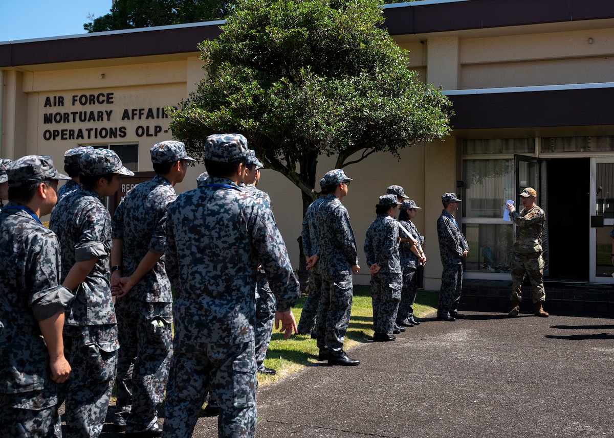 A U.S. military member greets Japan Air Self-Defense force members at the entrance of a building.