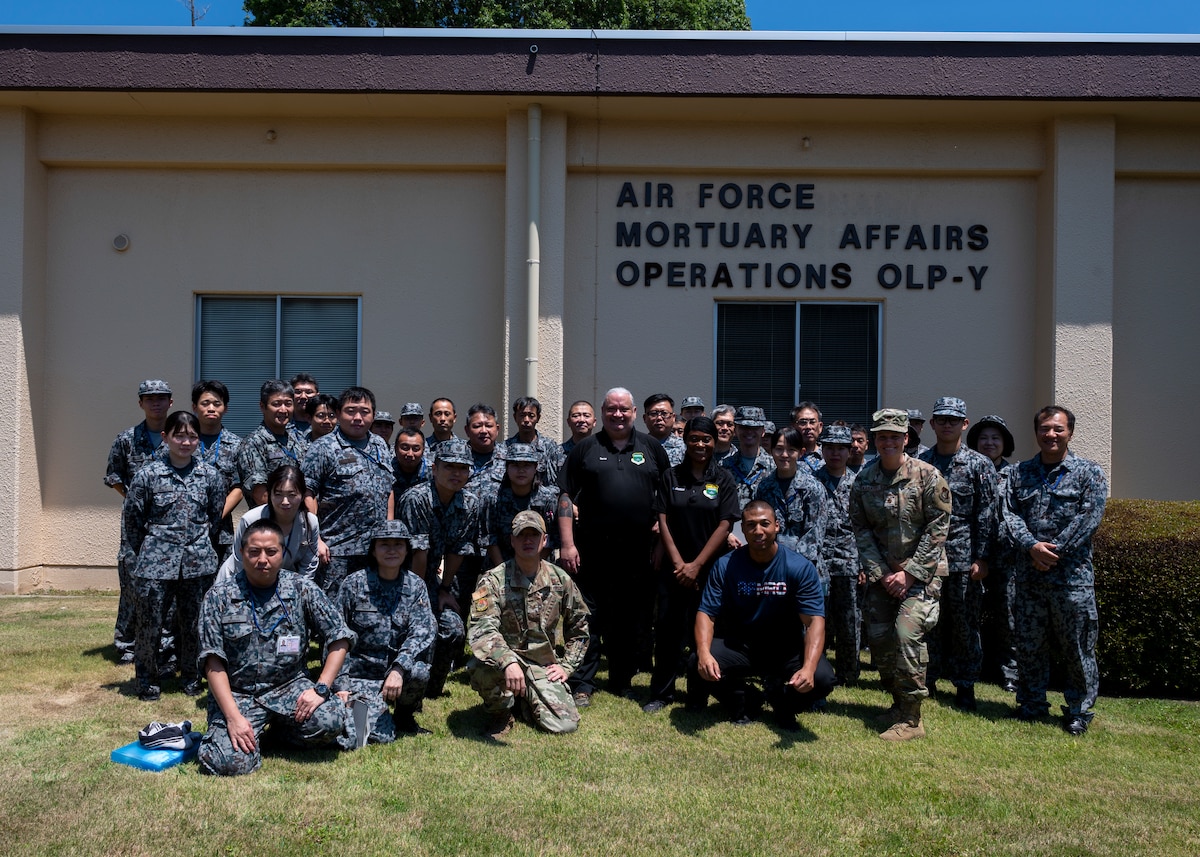 U.S. military members, civilians and Japan Air Self-Defense Force personnel pose for a photo in front of the Air Force Mortuary Affairs Operations building.