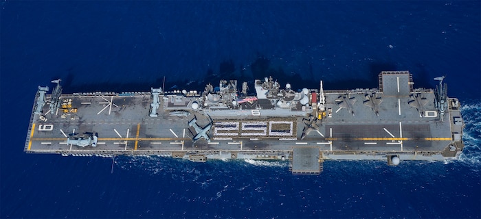 Sailors assigned to the forward-deployed amphibious assault ship USS America (LHA 6) and U.S. Marines with the 31st Marine Expeditionary Unit stand in formation for a photo commemorating 250 years of naval service, while conducting operations in the Coral Sea, Aug. 2.