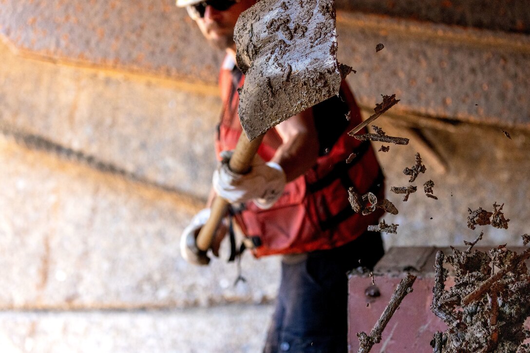 A crew member shovels debris aboard a working barge at a river lock.
